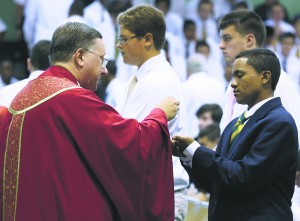 Father Walter Jenkins, president of Holy Cross H.S., shares the body of Christ with his students during the school’s opening liturgy. (Photo (C) Dominick Totino Photography)