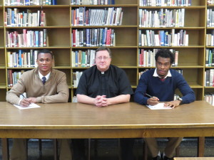 Holy Cross seniors Malachi Hoskins, left, and Lekeith Celestian, right, join Father Walter Jenkins, C.S.C., president, center, in signing their National Letters of Intent.