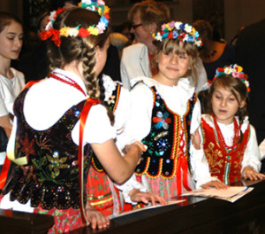 Girls dressed in Polish costumes exchange the sign of peace.
