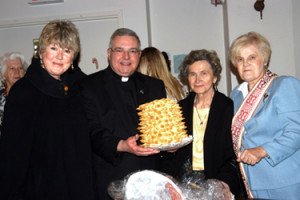 standing with members of the Lithuanian Apostolate, Msgr. Ronald Marino, president and vicar for migrant and ethnic apostolates, displays a traditional Lithuanian wedding cake.