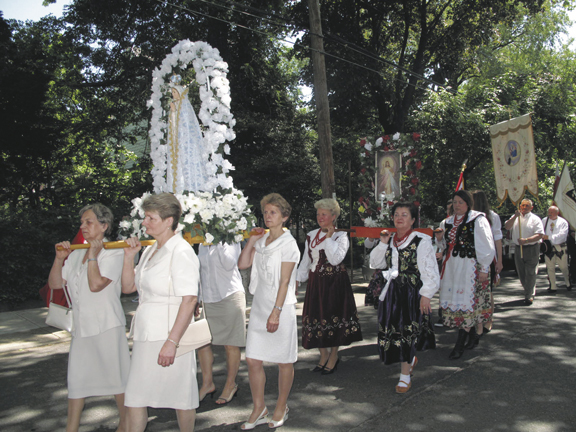 Women in the traditional Corpus Christi white carry a statue of Mary in procession. Behind them, women in traditional Polish garb carry an image of the Divine Mercy.