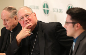 New York Cardinal Timothy M. Dolan listens to a question during a Sept. 11 press conference at the U.S. Conference of Catholic Bishops' headquarters in Washington. Also pictured is Bishop Richard E. Pates of Des Moines, Iowa, and Don Clemmer, USCCB assistant director of media relations. (Photo © Catholic News Service, Rob Roller)