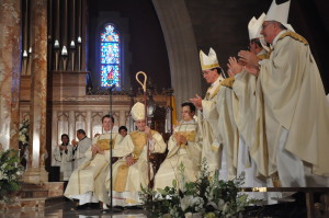 Archbishop Henry Mansell of Hartford, Conn., and Bishop Nicholas DiMarzio applaud as Bishop Frank Caggiano is seated on the “cathedra” or official seat of the Bishop of Bridgeport.