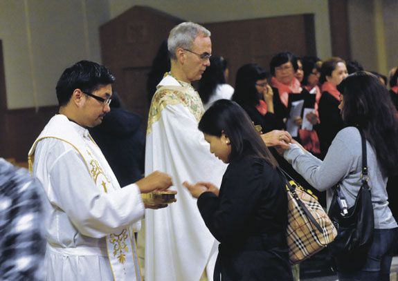 Bishop Paul Sanchez and Father Patrick Longalong distribute Communion during a Mass of healing for the Filipino community at St. Michael’s Church, Flushing.