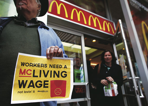 A woman exits a McDonald’s restaurant in New York Dec. 4 while members of the MoveOn organization shout slogans against the company in front of the restaurant. Fast-food workers staged strikes in about a hundred U.S. cities, most of which were Dec. 5, and held rallies in other places to demand higher wages.