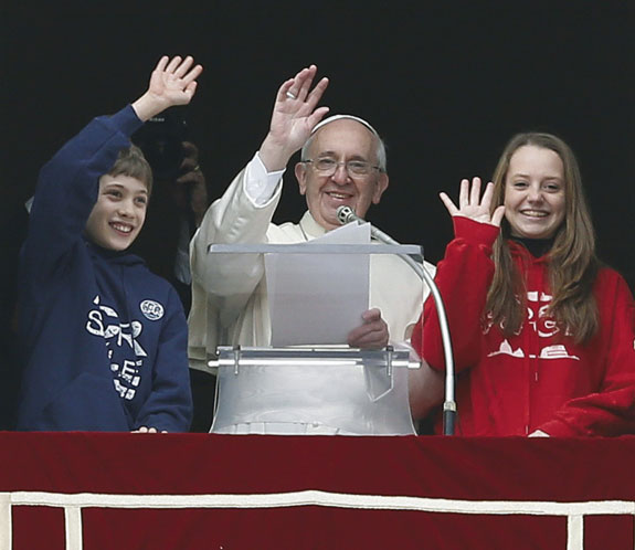 Pope Francis and young people wave from the window of his studio overlooking St. Peter’s Square at the Vatican Jan. 26. The two young people at his side launched doves to highlight the Church’s call for peace in the world.