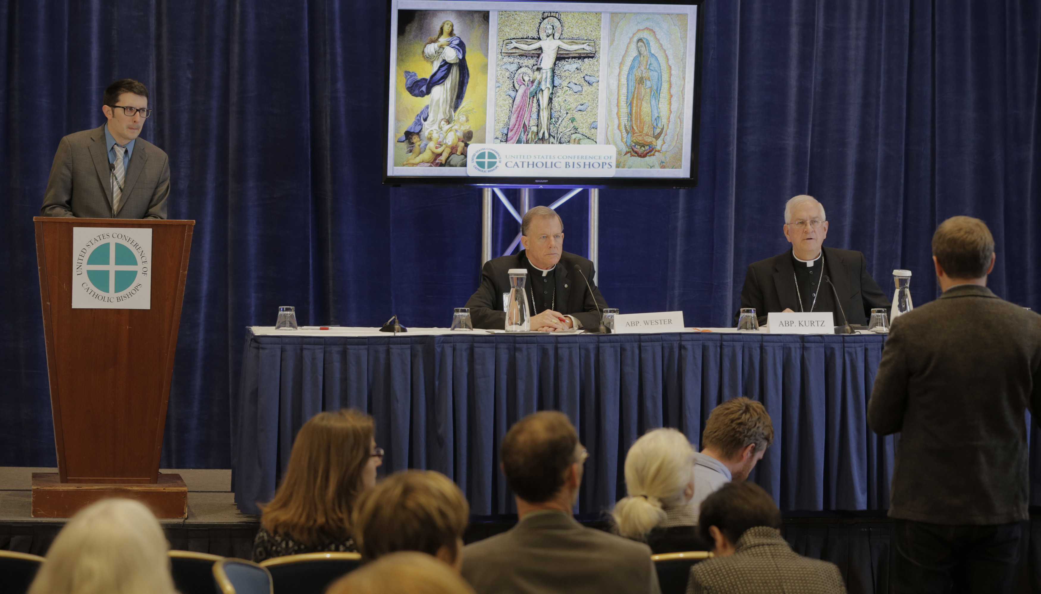A reporter asks a question Nov. 16 during a news conference at the 2015 fall general assembly of the U.S. Conference of Catholic Bishops in Baltimore. Pictured are Don Clemmer, USCCB assistant director of media relations, Archbishop John C. Wester of Santa Fe, N.M., and USCCB president, Archbishop Joseph E. Kurtz of Louisville, Ky. (Photo © Bob Roller)