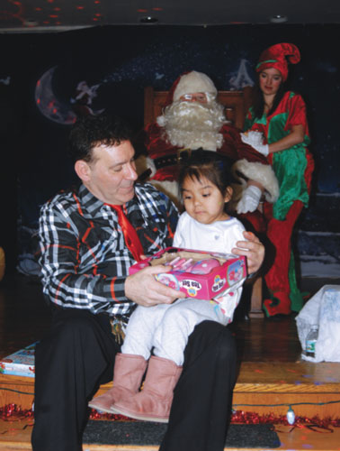 While Santa and his elf look on, real-life Santa Claus Thomas Neve hands a present to a young girl who attended one of two Operation Christmas Smiles events that helped bring cheer to 1,000 disadvantaged children last weekend. 