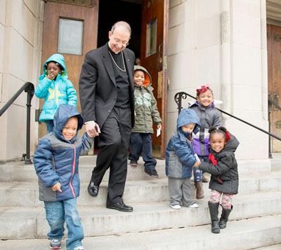 Archbishop William E. Lori of Baltimore walks with children after helping distribute 1,000 donated winter coats. (Photo by Catholic News Service/Olivia Obineme, Catholic Review) 