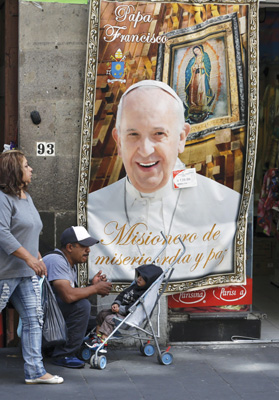 People walks past a Pope Francis banner outside a store in Mexico City. The Holy Father is visiting Mexico, Feb. 12-17. ( Photo © Catholic News Service/Henry Romero, Reuters)
