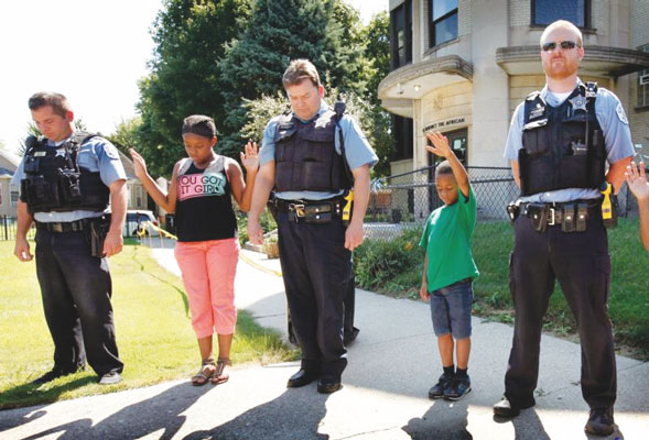 p Parents and schoolchildren in Chicago pray over members of the city’s police department during an Aug. 8 barbecue at the Academy of St. Benedict the African. The school held the event to thank local police for their support during the school year. (Photo: Catholic News Service/ Karen Callaway, Catholic New World)