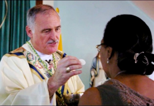 Bishop Tiedemann distributes Holy Communon to a resident of Mandeville, Jamaica.