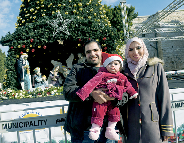 Muslim Palestinian Ashraf Natsheh, 28, holds his daughter Lara, 10 months, next to his wife, Shahad, 26, in front of the Christmas tree in Manger Square Dec. 5 in Bethlehem, West Bank. For more on Christmas in Bethlehem. Photo © Debbie Hill