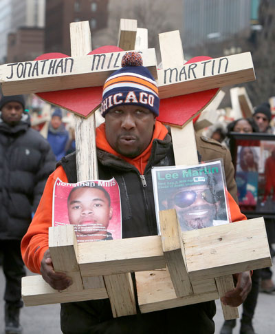 A man carries crosses with names of victims of gun violence during a march in downtown Chicago. Hundreds of people joined the march organized by Father Michael Pfleger, pastor of St. Sabina Parish on the city’s South Side, to remember those who died by gun violence in 2016. (Photo: Catholic News Service/Karen Callaway, Catholic New World)