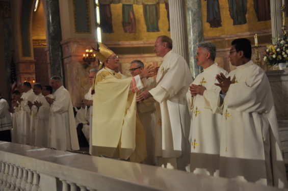 Bishop DiMarzio offers the sign of peace to Deacon John Hughes as Deacon Joseph Freda and Deacon Castellanos look on.