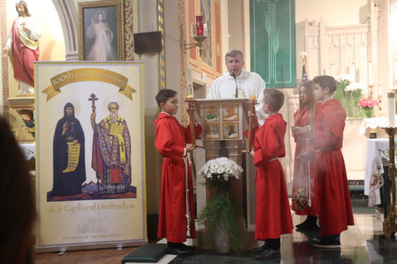 The pastor, Father Eugeniusz Kotlinski C.M, reads the gospel next to a banner depicting the parish’s patron saints.