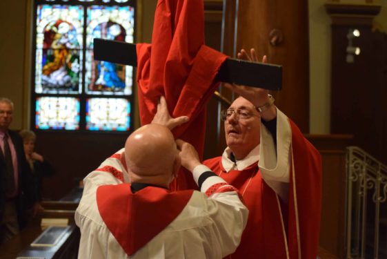 Bishop Nicholas DiMarzio and Father Anthony Sansone, pastor of Our Lady of the Miraculous Medal Church, Ridgewood, unfurl the cloth as they prepare for veneration of the cross at Good Friday’s services. (Photo Matthew O'Connor)