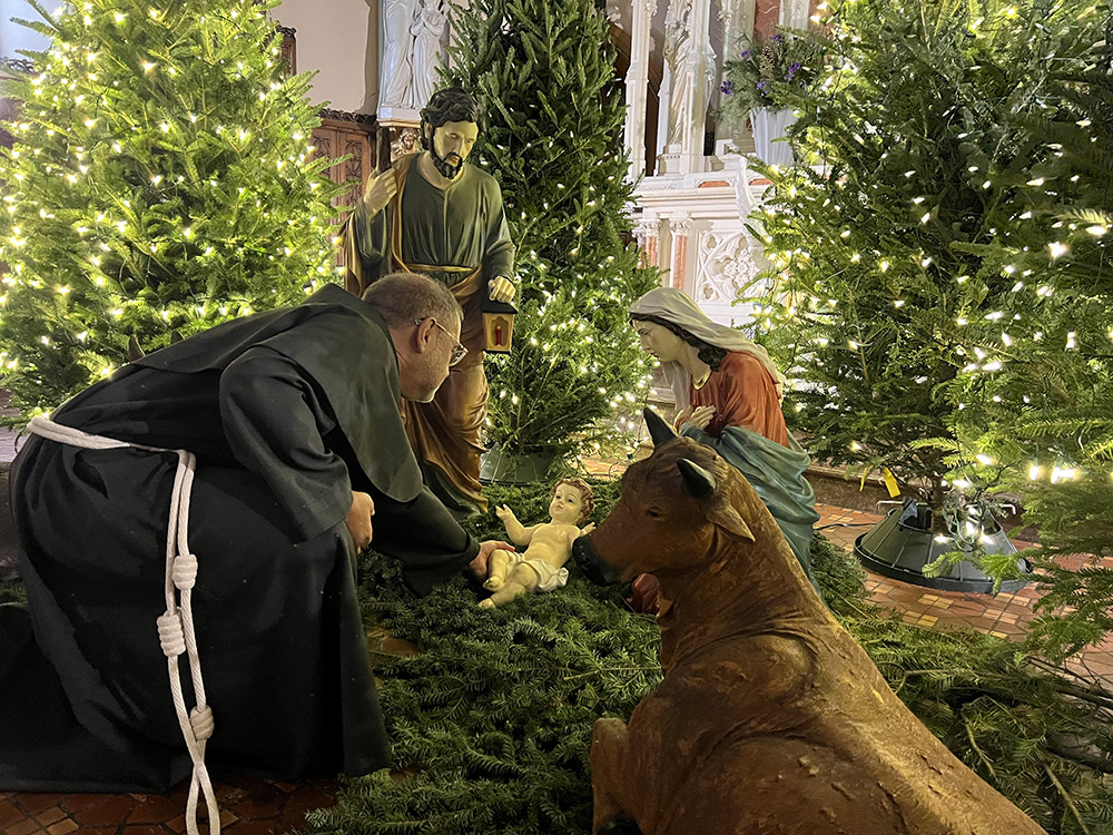 Friar Richard Riccioli placing the baby Jesus in the manger of the créche at Most Holy Trinity Church in Williamsburg. (Photo: Alicia Venter)